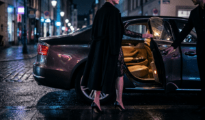 Mature woman in coat over lace entering a car held by a younger man's hand, capturing confident toy boy dating